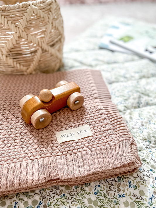 baby covered with pink blanket in brown woven basket with brown